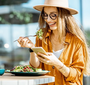 Woman smiling while looking at her phone and eating