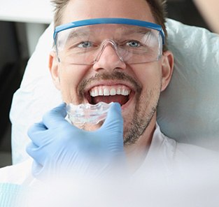 Dentist holding mouthguard to man’s teeth