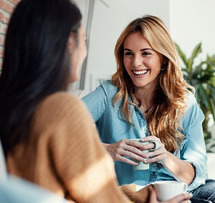 Woman smiling while drinking coffee with friend