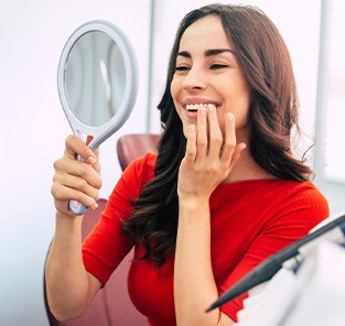 Woman smiling at reflection in handheld mirror