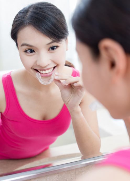Woman looking in mirror as she places a clear aligner