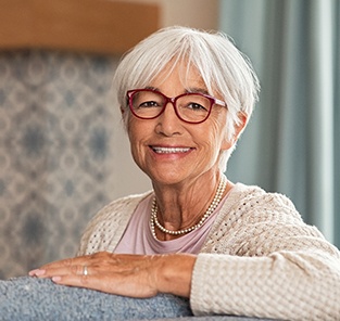 Senior woman with glasses leaning on couch and smiling