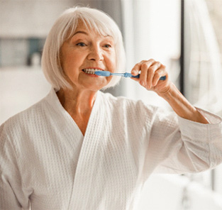 woman brushing teeth after getting dental implants in Norton Shores