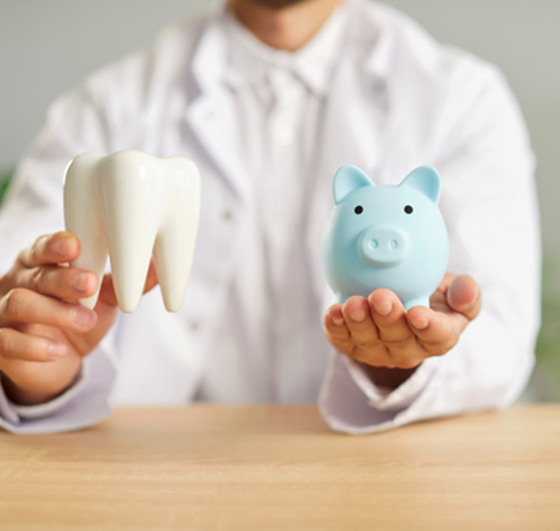 Dentist in white coat holding a model tooth and blue piggy bank
