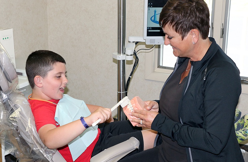 Dental team member showing young boy patient a model of the smile in Norton Shores