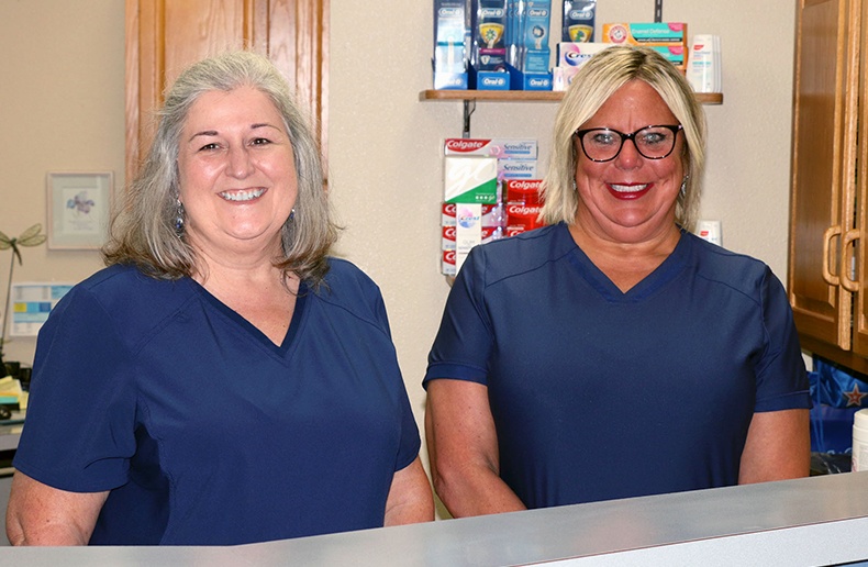 Two Norton Shores dental team members smiling behind front desk