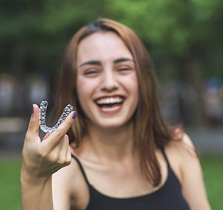 Young woman laughing and holding Invisalign in Norton Shores, MI