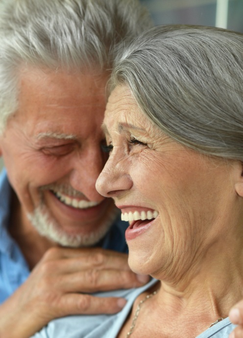 Man and woman smiling after replacing missing teeth