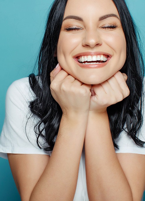 Woman smiling with eyes closed and hands in fists under her chin