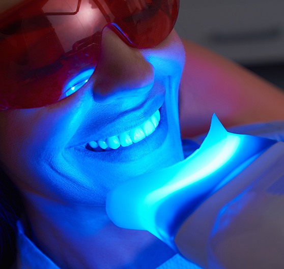 Closeup of woman in dental chair with UV light applied to teeth whitening