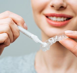 Woman applying whitening gel to custom-fitted applicator