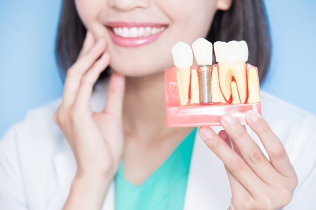dentist touching cheek and holding dental implant model