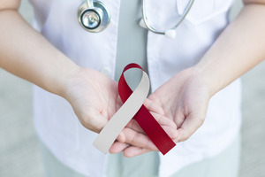 Holding a red and white ribbon for oral cancer awareness