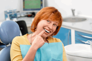 Patient smiling in treatment chair and pointing to her natural teeth